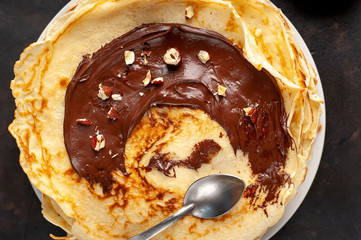 Pancakes with chocolate paste and hazelnuts, on a white plate on a background of concrete, slate