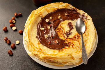Pancakes with chocolate paste and hazelnuts, on a white plate on a background of concrete, slate
