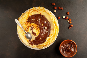 Pancakes with chocolate paste and hazelnuts, on a white plate on a background of concrete, slate