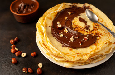 Pancakes with chocolate paste and hazelnuts, on a white plate on a background of concrete, slate