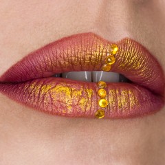 Beautiful female lips closeup. Red lipstick, gold paint. Jewellery on lips