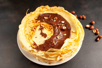 Pancakes with chocolate paste and hazelnuts, on a white plate on a background of concrete, slate