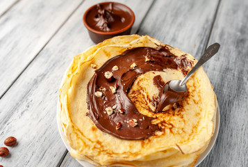 Pancakes with chocolate spread and hazelnuts,  on a white plate on a wood background