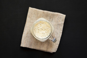Banana smoothie in a glass jar mug on a black background, top view. Flat lay, overhead, from above. Close-up.