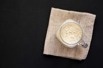 Banana smoothie in a glass jar mug on a black surface, top view. Flat lay, overhead, from above. Copy space.