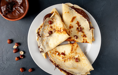 Pancakes with chocolate paste and hazelnuts, on a white plate on a background of concrete, slate