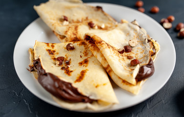 Pancakes with chocolate paste and hazelnuts, on a white plate on a background of concrete, slate