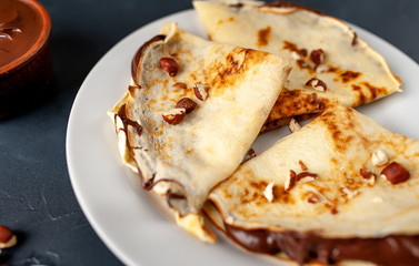 Pancakes with chocolate paste and hazelnuts, on a white plate on a background of concrete, slate