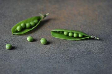 Two pods of fresh young green peas on a gray background. Separate pea on the surface. Close-up.