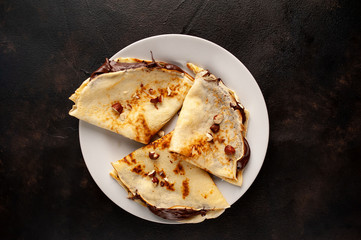 Pancakes with chocolate paste and hazelnuts, on a white plate on a background of concrete, slate