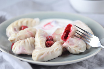 Dumplings with cherries and sour cream. Half dumplings impaled on a fork. Light background. Close-up.