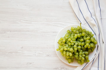 Green grape on a white plate over white wooden background, top view. Copy space.