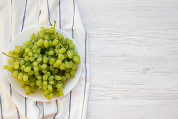 Green grape on a white plate on a white wooden surface, top view. Overhead, from above. Copy space.