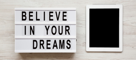 'Believe in your dreams' word on a lightbox, tablet with blank screen over white wooden surface, top view. Overhead, flat lay, from above.