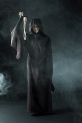 full length view of woman in death costume holding hanging noose in smoke on black