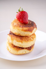 Cottage cheese pancakes with one strawberry on white plate isolated angle view