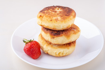 Cottage cheese pancakes with one strawberry on white plate isolated angle view