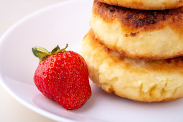 Cottage cheese pancakes with one strawberry on white plate isolated angle view