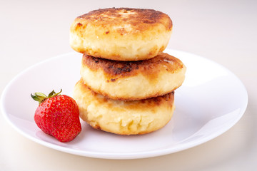 Obraz na płótnie Canvas Cottage cheese pancakes with one strawberry on white plate isolated angle view