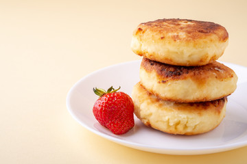 Cottage cheese pancakes with one strawberry on white plate on yellow background isolated angle view