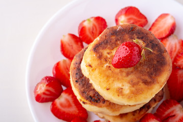 Cottage cheese pancakes with sliced strawberries on white plate isolated