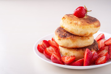 Cottage cheese pancakes with sliced strawberries on white plate isolated