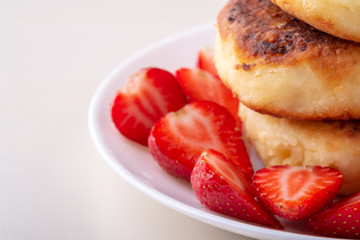 Cottage cheese pancakes with sliced strawberries on white plate isolated