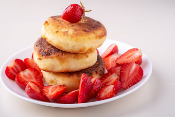 Obraz na płótnie Canvas Cottage cheese pancakes with sliced strawberries on white plate isolated