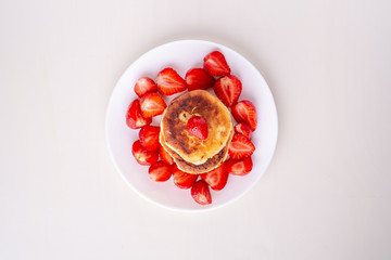 Cottage cheese pancakes with sliced strawberries on white plate isolated