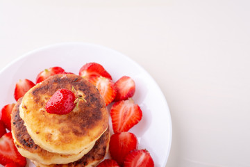 Cottage cheese pancakes with sliced strawberries on white plate isolated