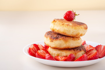 Cottage cheese pancakes with sliced strawberries on white plate isolated