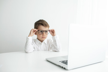 Cute little boy using laptop while doing homework against white background