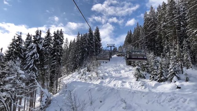 FPV: Riding a chairlift uphill in a ski resort in Flachau, Austria with a blue sky and lots of snow
