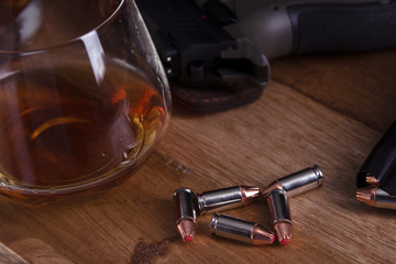 gun and glass of cognac on wooden table