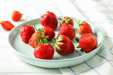 Plate with fresh strawberries and kitchen towel on white wooden background, closeup and space for text