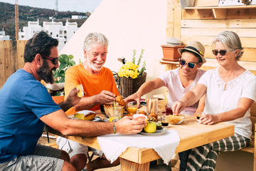 Adult people and one teenager smiling and eating. Multi generation family enjoy breakfast together. Senior couple with son and nephew. Wooden table and background