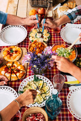 Four adult people enjoying meal together. Red checkered tablecloth in the table outdoor in the terrace. Wooden cutting board with pizza. Vegetables and eggs. Fresh natural fruits