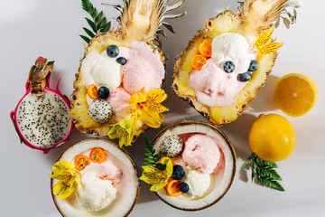 Balls of ice cream decoration flowers and berries in halves of coconut and  pineapple. Summer tropical concept.
