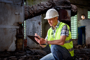 A man in a construction helmet and with a black folder in his hands at a construction site. Brigadier in working form, inspection of the structure. A man takes notes.