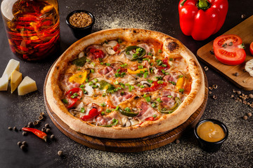 Concept Italian cuisine. A real pizza with vegetables and ham, bacon and parmesan cheese. The ingredients on the table. Red wine in a glass on the table. Closeup, background image