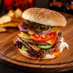 American cuisine concept. A large homemade burger with a double pork and veal meat patty, tomato, cucumber, lettuce, and cheese. Closeup, background image