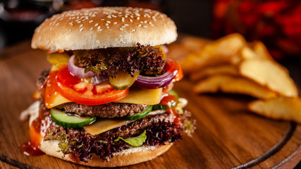American cuisine concept. A large homemade burger with a double pork and veal meat patty, tomato, cucumber, lettuce, and cheese. Closeup, background image