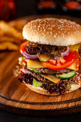 American cuisine concept. A large homemade burger with a double pork and veal meat patty, tomato, cucumber, lettuce, and cheese. Closeup, background image