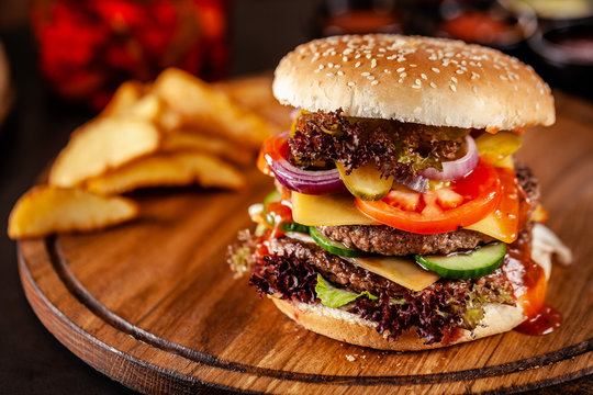 American cuisine concept. A large homemade burger with a double pork and veal meat patty, tomato, cucumber, lettuce, and cheese. Closeup, background image