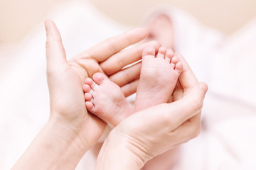 Obraz na płótnie Canvas Mother holding newborn baby feet in hands. Mom taking care about infant child after taking bath. Parents childcare. Children healthcare and happy family