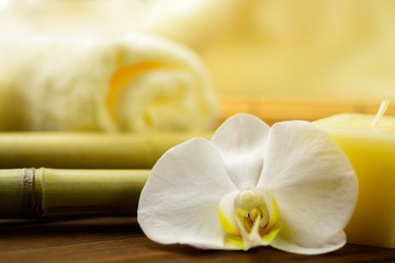 Spa towels, candle and orchid on bamboo blurred background.