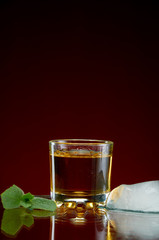 Glass with alcohol in a transparent glass with ice and mint on a red background