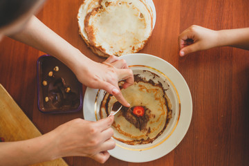 A little boy with his mother preparing together a breakfast. Mother and son smearing chocolate cream to thin pancakes. Free space