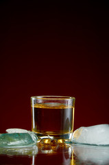 Strong alcoholic drink in a transparent glass with ice on a red background
