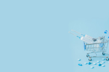 Pills and medical injection in shopping trolley on blue background. Creative idea for health care cost, drugstore, health insurance and pharmaceutical company business concept. Copy space